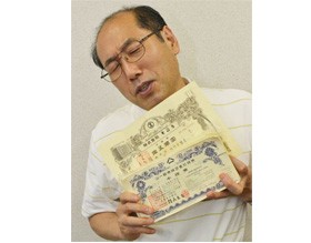<桐谷さん画像>紙切れになった株券を持ち苦笑いをする、株主優待で話題の桐谷さんこと桐谷広人氏。“先読み投資力”を鍛える方法を解説!